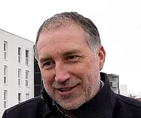 Porträt eines Mannes mit dunkler Jacke im Freien vor einer modernen Wohnanlage mit sybkon Balkonen in Schwanenstadt