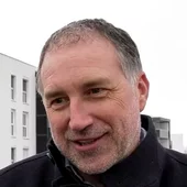 christian-smrcka-wien-sued-florianigasse-referenz-innovametall.webp Porträt eines Mannes mit dunkler Jacke im Freien vor einer modernen Wohnanlage mit sybkon Balkonen in Schwanenstadt