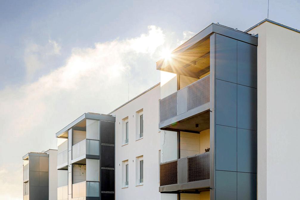 Mehrparteienhaus mit modernen sybkon Balkonen aus Metall, Photovoltaik Modulen und Glas bei Sonnenschein