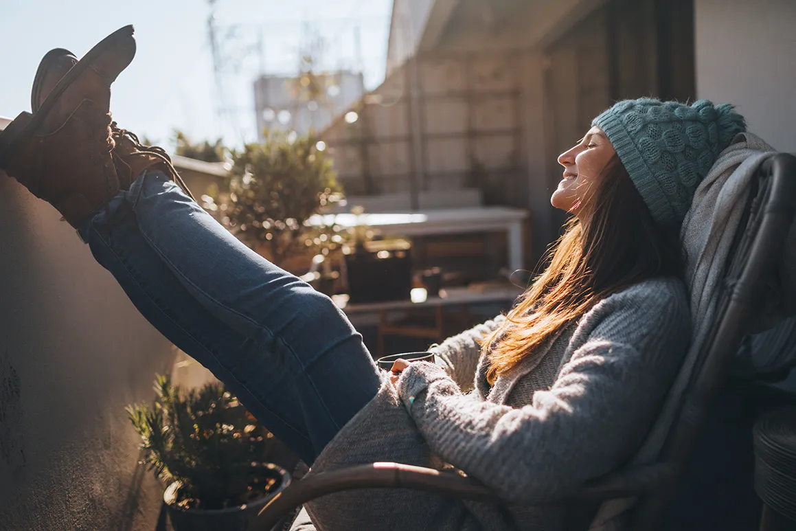 Frau genießt die Sonne auf einem Balkon im Winter